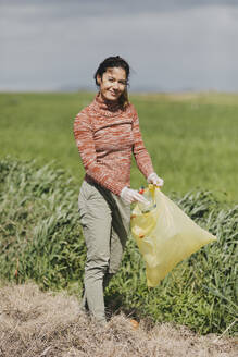 Smiling woman collecting bottles at countryside - DMGF01320