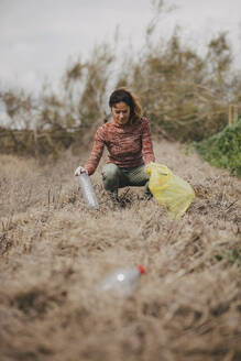 Woman crouching and collecting plastic bottles at countryside - DMGF01325