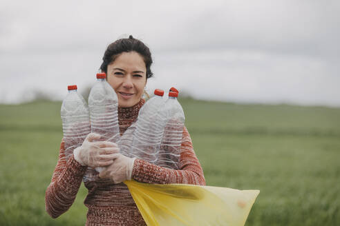 Frau mit Plastikhandschuhen und Flaschen in der Hand auf dem Land - DMGF01329
