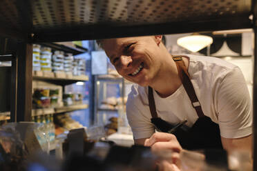 Smiling baker working near shelf in bakery - ASGF04957