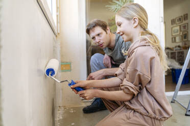 Smiling girl painting wall near father at home - NJAF00942