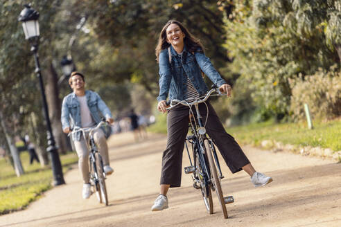 Carefree woman cycling with boyfriend at park - JSRF02993