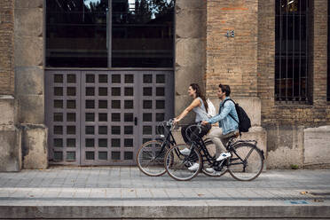 Couple cycling near building entrance on sidewalk - JSRF02996