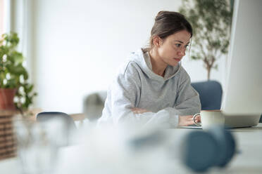 Selbstbewusste Geschäftsfrau mit Laptop am Tisch, die von zu Hause aus arbeitet - KNSF10257