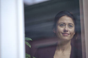 Thoughtful smiling businesswoman looking out through window at home office - KNSF10280
