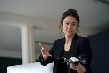 Confident businesswoman holding drone gesturing at home office - KNSF10286