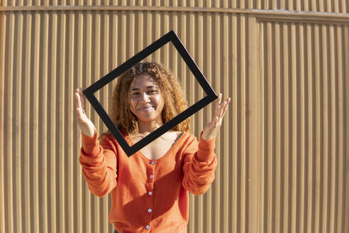 Black girl with curly hair posing and playing with a photo frame. Granada, Spain. - MGRF01130