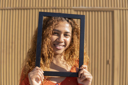 Black girl with curly hair posing and playing with a photo frame. Granada, Spain. - MGRF01135