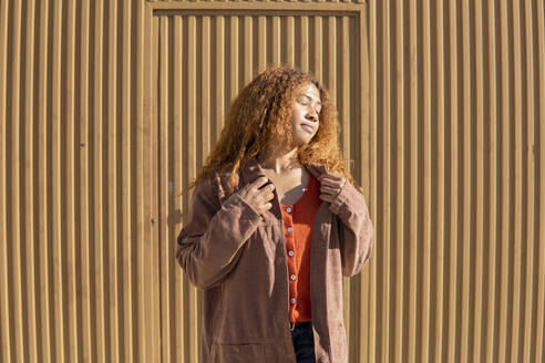 Junge Frau in Jacke mit geschlossenen Augen vor einer Metallwand stehend - MGRF01139