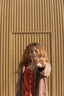 Glückliche junge Frau mit Metallstern vor einer Wand - MGRF01140