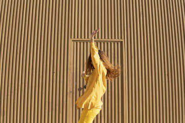 Junge Frau genießt den Tanz vor einer Metallwand an einem sonnigen Tag - MGRF01161