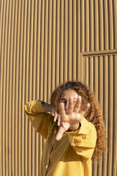 Junge Frau tanzt mit verdunkeltem Gesicht vor einer orangefarbenen Wand - MGRF01167