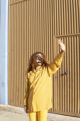 Junge Frau in gelber Freizeitkleidung, die ihre Augen mit der Hand abschirmt, an einem sonnigen Tag - MGRF01168