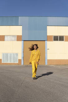 Black girl with curly hair dressed in yellow pants and shirt, walking and smiling relaxed. Granada, Spain. - MGRF01170