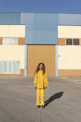Junge Frau in gelber Freizeitkleidung steht auf dem Fußweg - MGRF01171