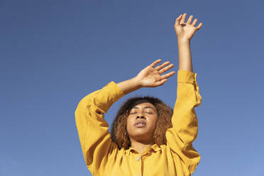 Junge Frau mit erhobenen Händen und geschlossenen Augen an einem sonnigen Tag - MGRF01183