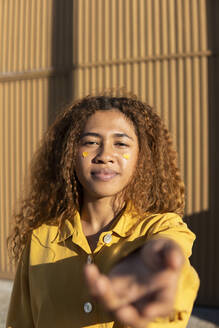 Black girl with curly hair dressed in yellow pants and shirt, posing with yellow hearts stuck on her cheeks. Granada, Spain. - MGRF01193