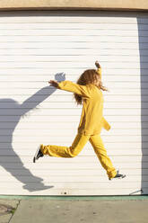 Aufgeregte junge Frau, die vor einem weißen Fensterladen springt - MGRF01204