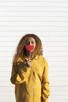 Black girl with curly hair dressed in yellow pants and shirt, posing with a red heart. Granada, Spain. - MGRF01213