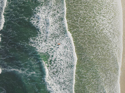 Luftaufnahme von Surfern im Meer, die durch die Wellen in Peniche, Portugal, laufen. - AAEF28448