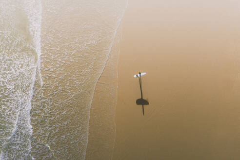 Luftaufnahme eines Surfers und seines Schattens an einem goldenen Strand in Peniche, Portugal. - AAEF28451