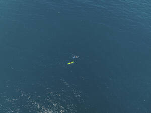 Aerial view of a two tiny people canoeing into the sea in Milazzo, Sicily, Italy. - AAEF28647