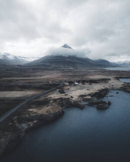 Aerial view of a solitary road winding toward a coastal mountain under overcast skies, Austurland, Iceland. - AAEF28777