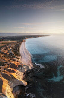 Luftaufnahme von zerklüfteten Kalksteinklippen mit einem türkisblauen Meer im Vordergrund und einem weißen Sandstrand bei Sonnenuntergang, Port Willunga, Südaustralien, Australien. - AAEF29046
