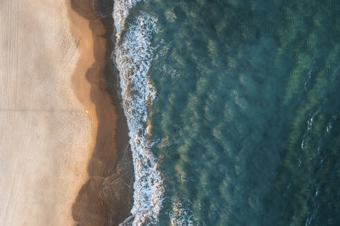 Luftaufnahme eines Sandstrandes von oben mit türkisblauem Wasser, einer am Strand stehenden Person und anrollenden Wellen, Port Noarlunga, South Australia, Australien. - AAEF29049