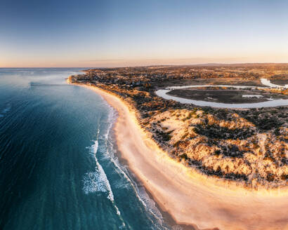 Aerial View over a long sandy stretch of beach during sunset, with blue water waves rolling onto shore, Port Noarlunga, South Australia, Australia. - AAEF29050
