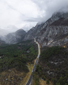 Luftaufnahme eines nebligen Tals mit kurvenreicher Straße und Berggipfel, Trentino, Italien. - AAEF29259