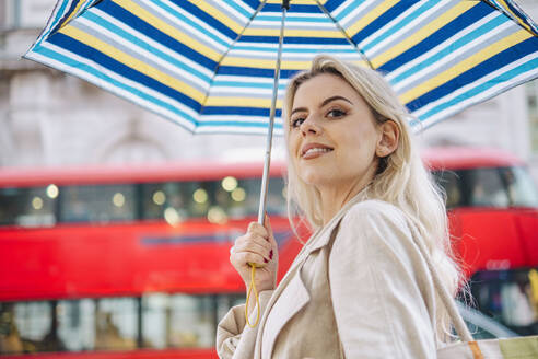 Glückliche junge Frau mit Regenschirm in der Nähe des roten Busses - AMWF02091