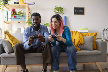 Lächelnde Freunde spielen ein Videospiel auf dem Sofa zu Hause - JCCMF11599