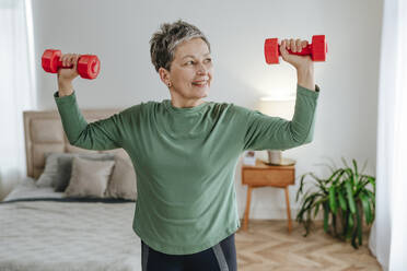 Smiling woman exercising with dumbbells at home - YTF02087