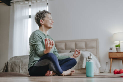 Lächelnde Frau übt Yoga auf einer Matte sitzend zu Hause - YTF02094