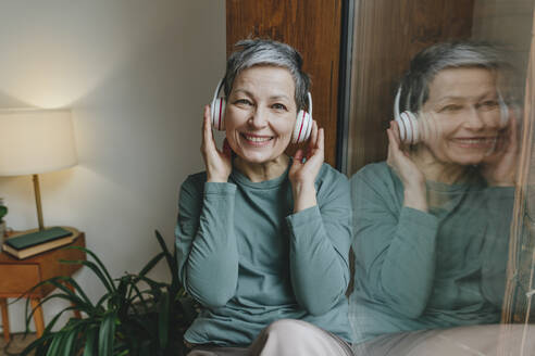 Glückliche Frau, die zu Hause über drahtlose Kopfhörer Musik hört - YTF02120