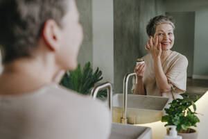 Lächelnde Frau bei der Hautpflege im Spiegel zu Hause - YTF02126