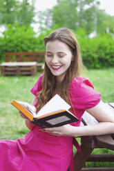 Smiling woman enjoying reading book at park - YHF00123