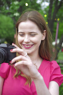 Lächelnde Frau, die im Park Bilder mit der Kamera aufnimmt - YHF00126
