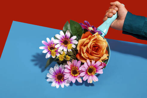Hand eines Mannes hält Bratpfanne mit bunten Blumen vor farbigem Hintergrund - RDTF00101
