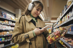 Frau benutzt Smartphone, um Informationen über ein Produkt im Supermarkt zu überprüfen - ALKF01152