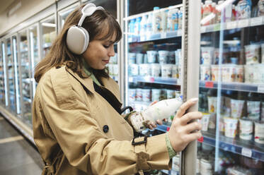 Junge Frau liest die Produktbeschreibung auf einer Milchflasche im Supermarkt - ALKF01157