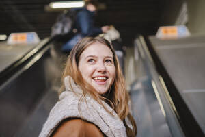 Glückliche junge Frau, die auf einer Rolltreppe in der U-Bahn nach oben fährt - AMWF02094
