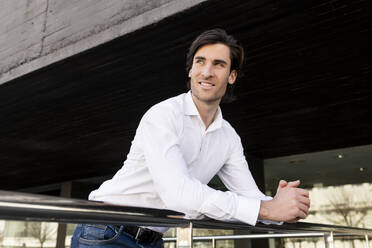 Smiling young businessman leaning on railing - LMCF01004