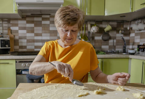 Ältere Frau bei der Zubereitung von Gebäck mit Teig in der Küche zu Hause - MBLF00351