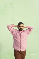 Mann stehend mit Kopf in den Händen vor einer mintgrünen Wand - MGRF01247