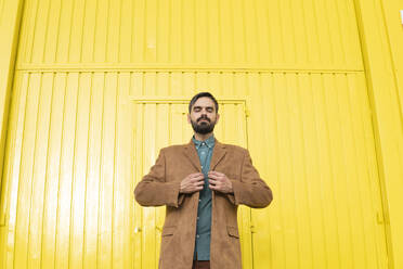 Mann mit brauner Jacke und vor gelber Wand stehend - MGRF01257