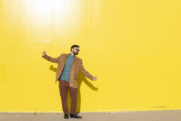 Mann mit Sonnenbrille und tanzend vor einer gelben Wand - MGRF01275