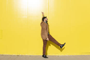 Fröhlicher Mann tanzt vor einer gelben Wand - MGRF01282