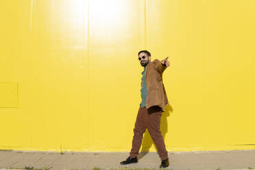Glücklicher Mann mit Sonnenbrille und tanzend vor einer gelben Wand - MGRF01283